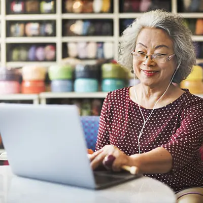 an elderly woman with grey hair using headphones and working on a laptop
