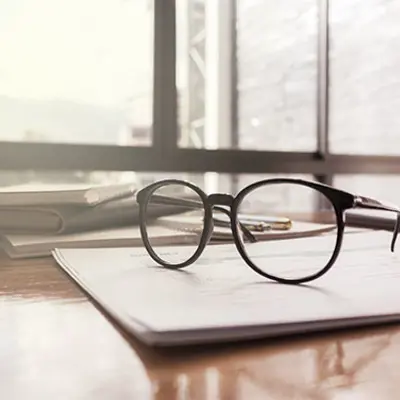 a pair of glasses on top of a notepad on a table with windows in the background