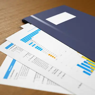 a navy blue folder on a table and sheets of paper underneath it with tables and charts 